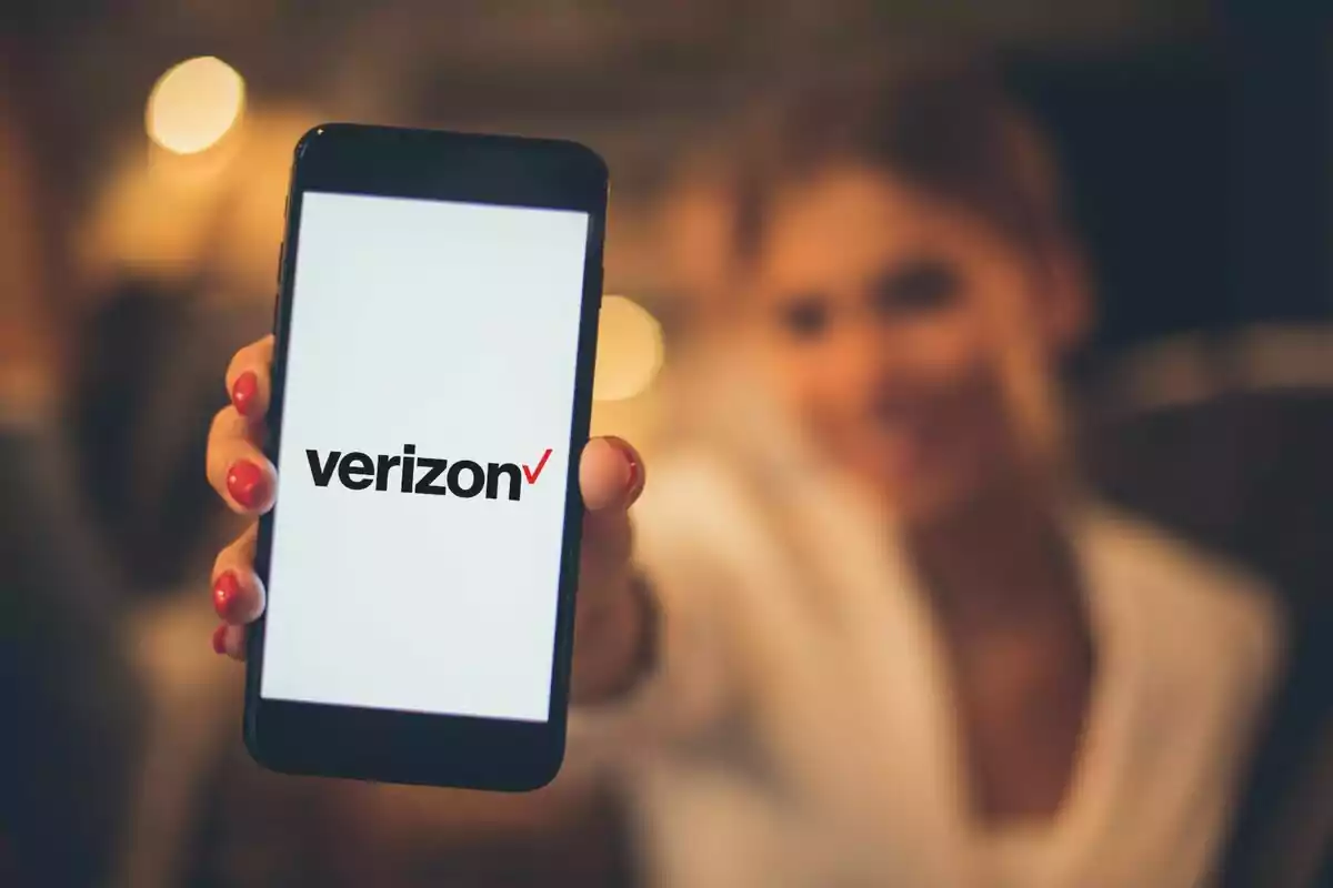 Persona sosteniendo un teléfono móvil que muestra el logo de Verizon en la pantalla. Persona sosteniendo un teléfono móvil que muestra el logo de Verizon en la pantalla.