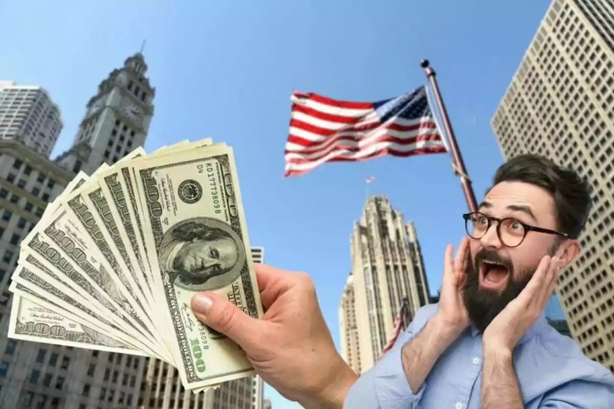 A man with a surprised expression looks at a fan of hundred-dollar bills in an urban setting with tall buildings and a waving United States flag in the background.