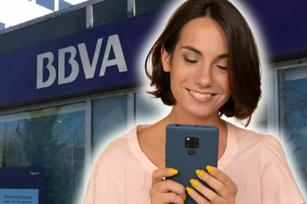 Una dona somrient amb un telèfon mòbil davant d'un edifici del BBVA.