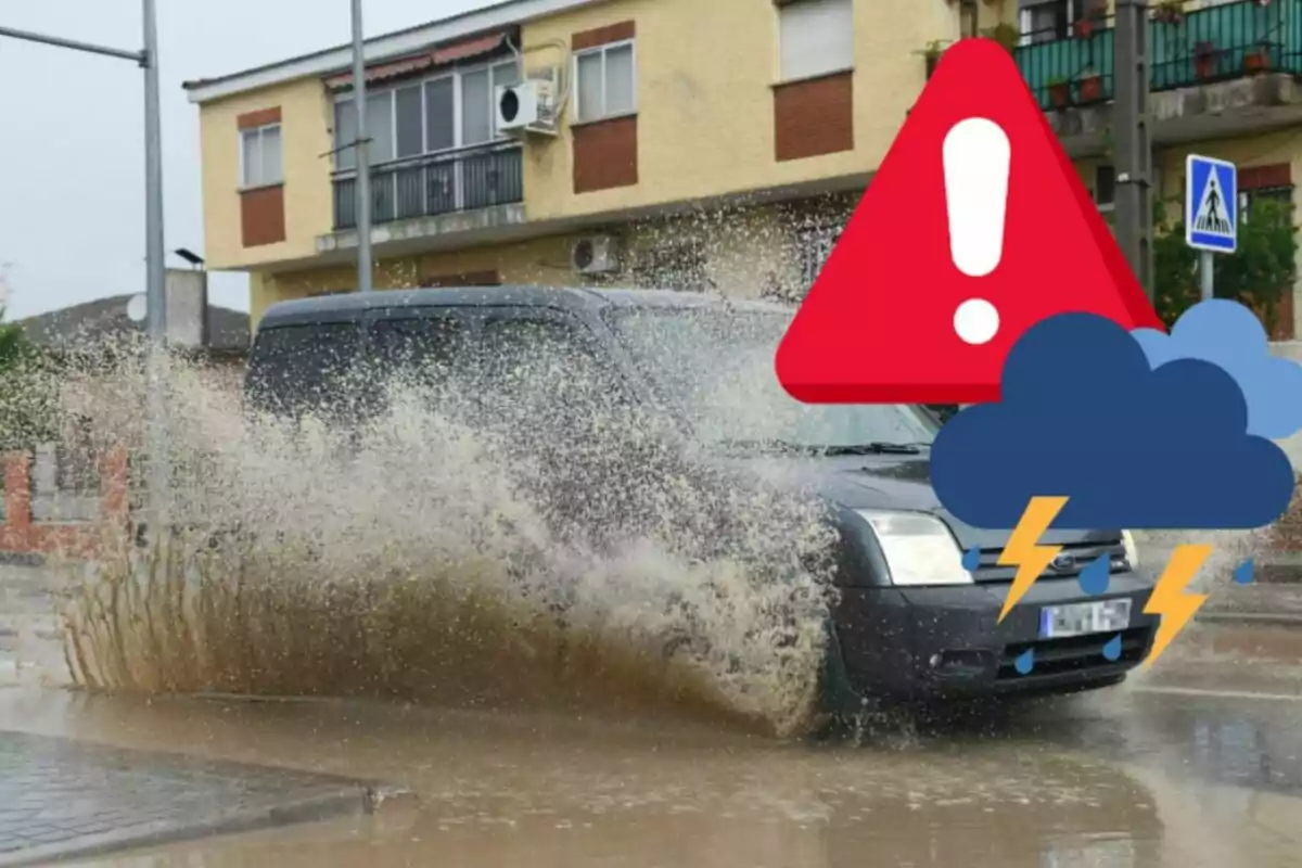 Un cotxe negre esquitxant aigua mentre passa per un bassal gran en un carrer residencial durant una tempesta.