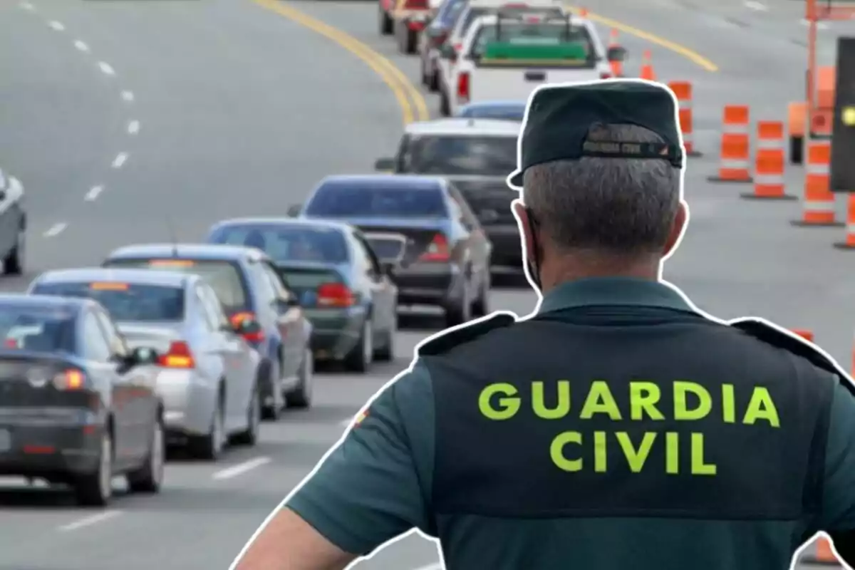 Un agente de la Guardia Civil observa una fila de coches en una carretera con conos de tráfico.