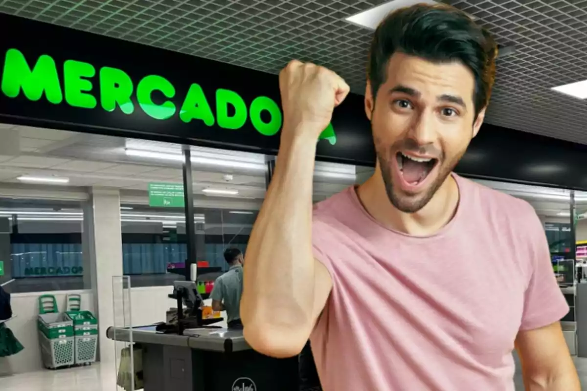Hombre joven sonriente y levantando el puño en señal de alegría frente a la entrada de un supermercado Mercadona