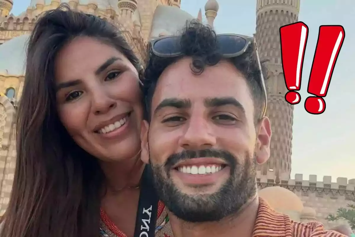 Isa Pantoja y Asraf Beno sonriente se toma una selfie frente a un edificio con arquitectura detallada y un par de signos de exclamación rojos en la esquina.