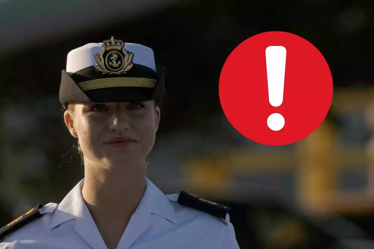 Leonor amb uniforme militar i un barret blanc amb insígnies, al costat d'una icona d'exclamació en un cercle vermell.