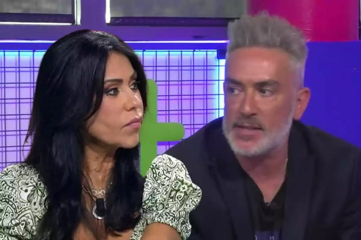 Maite Galdeano i Kiko Hernández conversant en un set de televisió amb fons colorit.