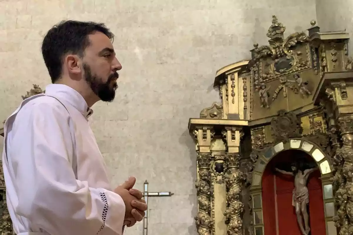 Un home amb vestimenta religiosa blanca està de perfil en una església amb un altar ornamentat al fons. Un home amb vestimenta religiosa blanca està de perfil en una església amb un altar ornamentat al fons.