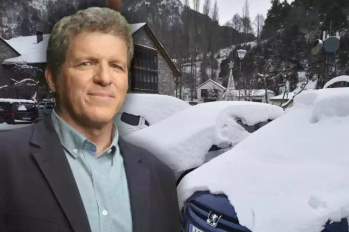 Un hombre de pie frente a un paisaje invernal con coches cubiertos de nieve y montañas al fondo.