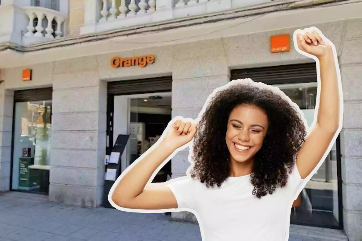 Mujer sonriente con los brazos levantados frente a una tienda de Orange.