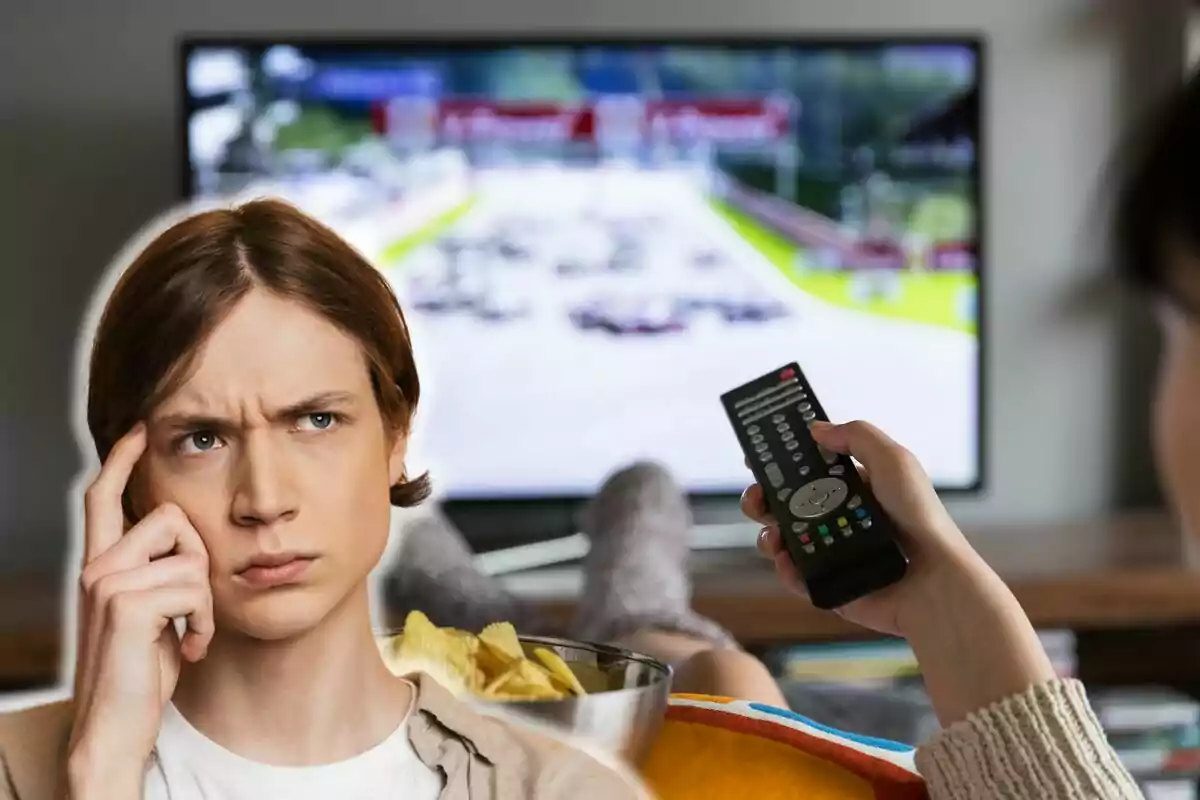 Una persona pensativa con un bol de papas fritas mientras otra sostiene un control remoto frente a un televisor que muestra una carrera de autos.