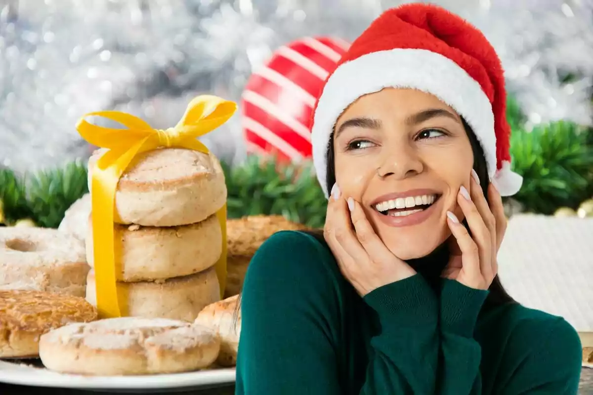 Una persona somrient amb una gorra de Nadal al costat d'una pila de galetes decorades amb un llaç groc, amb un fons festiu.