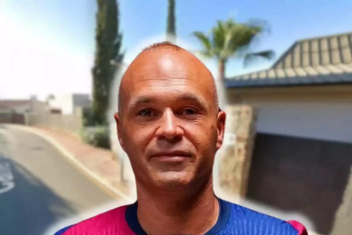 Andrés Iniesta amb samarreta blava i vermella posant davant un carrer amb arbres i cases al fons.