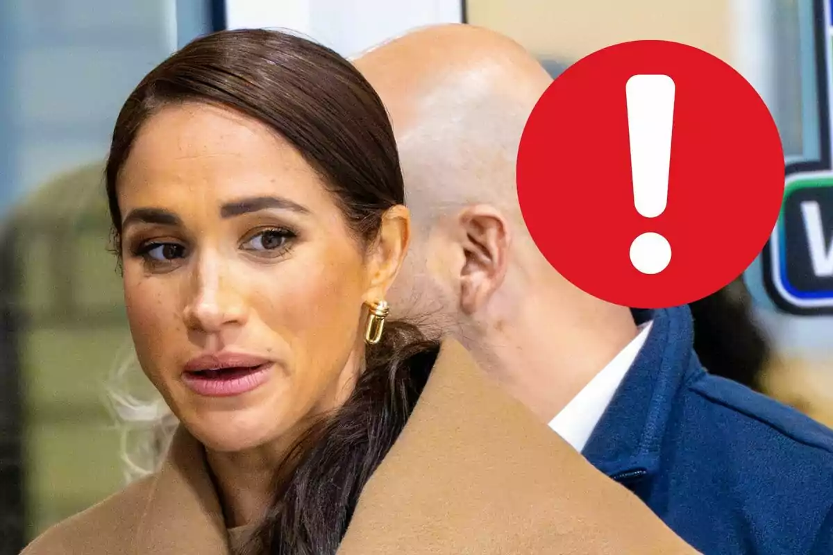 Meghan Markle with dark hair and a beige coat stands in a public place, while a red circle with an exclamation mark partially covers another person in the background.