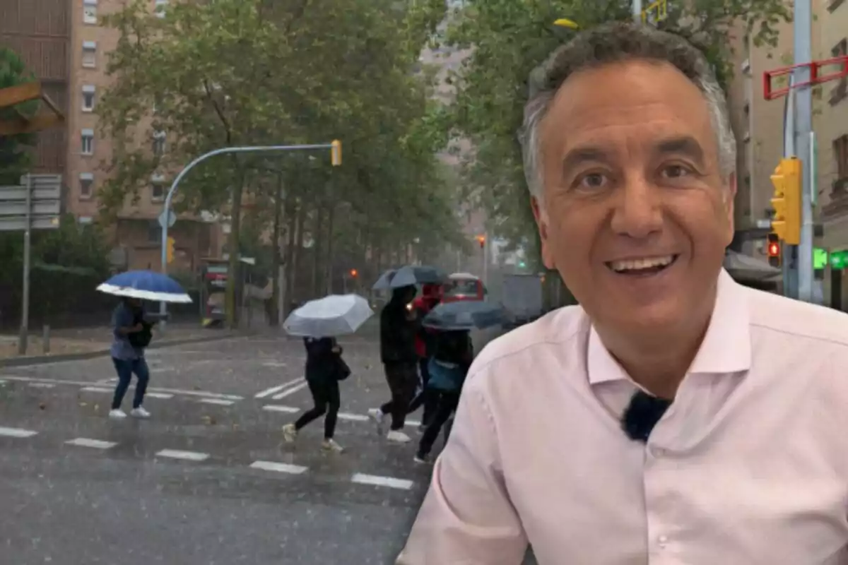 Una persona somrient en primer pla amb un fons de persones creuant el carrer sota la pluja amb paraigües.