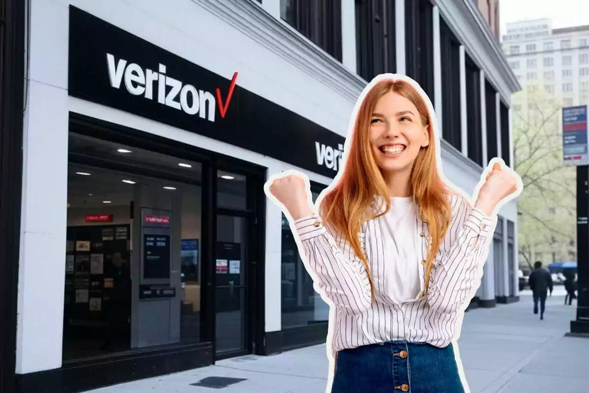 A smiling woman with her fists raised is in front of a Verizon store on a city street. A smiling woman with her fists raised is in front of a Verizon store on a city street.