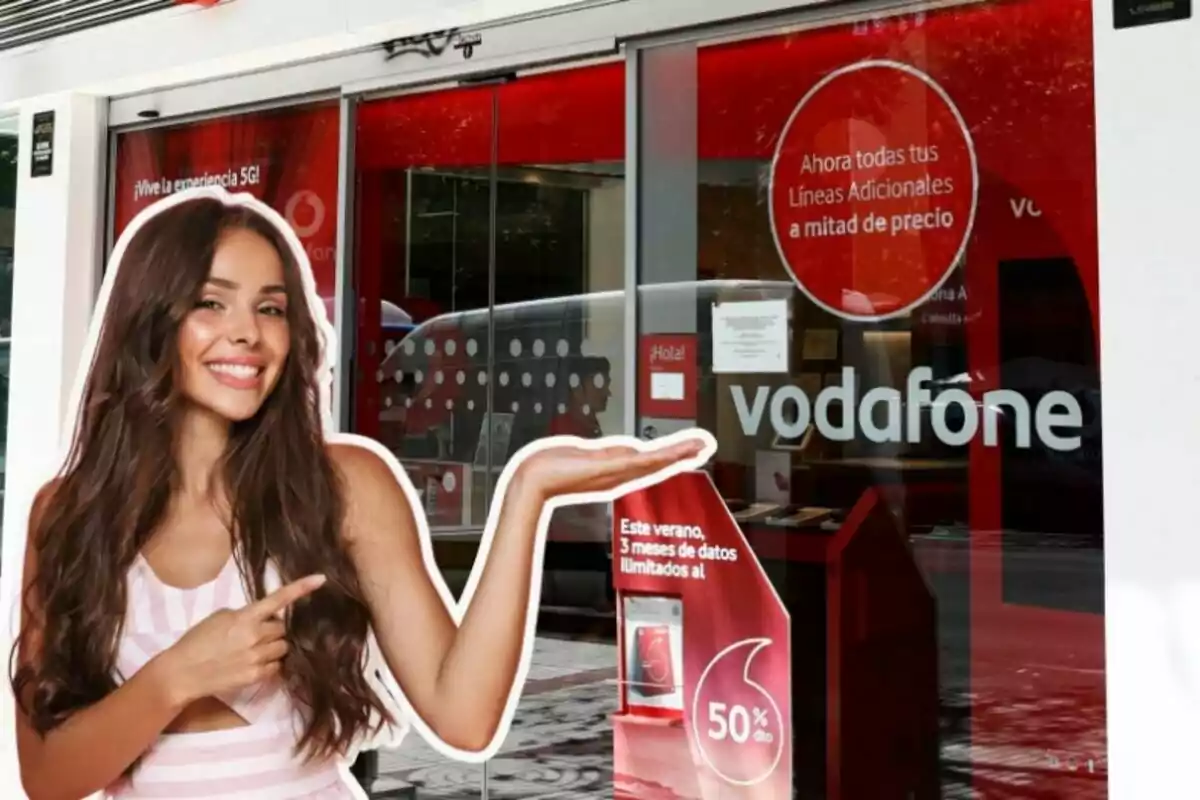 Una dona somrient assenyala cap a un cartell promocional de Vodafone a l'entrada d'una botiga, destacant una oferta de línies addicionals a meitat de preu i dades il·limitades durant l'estiu.