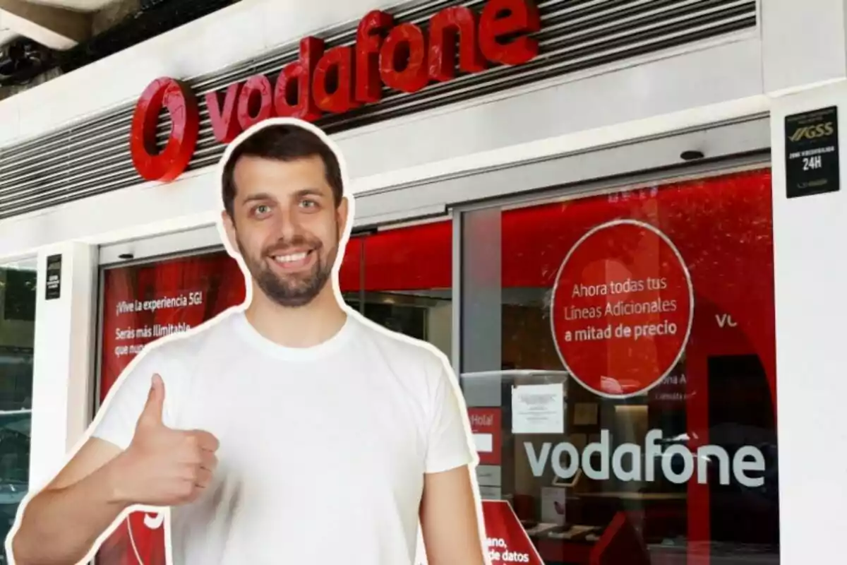 Un home somrient amb una samarreta blanca i el polze cap amunt és davant d'una botiga de Vodafone.