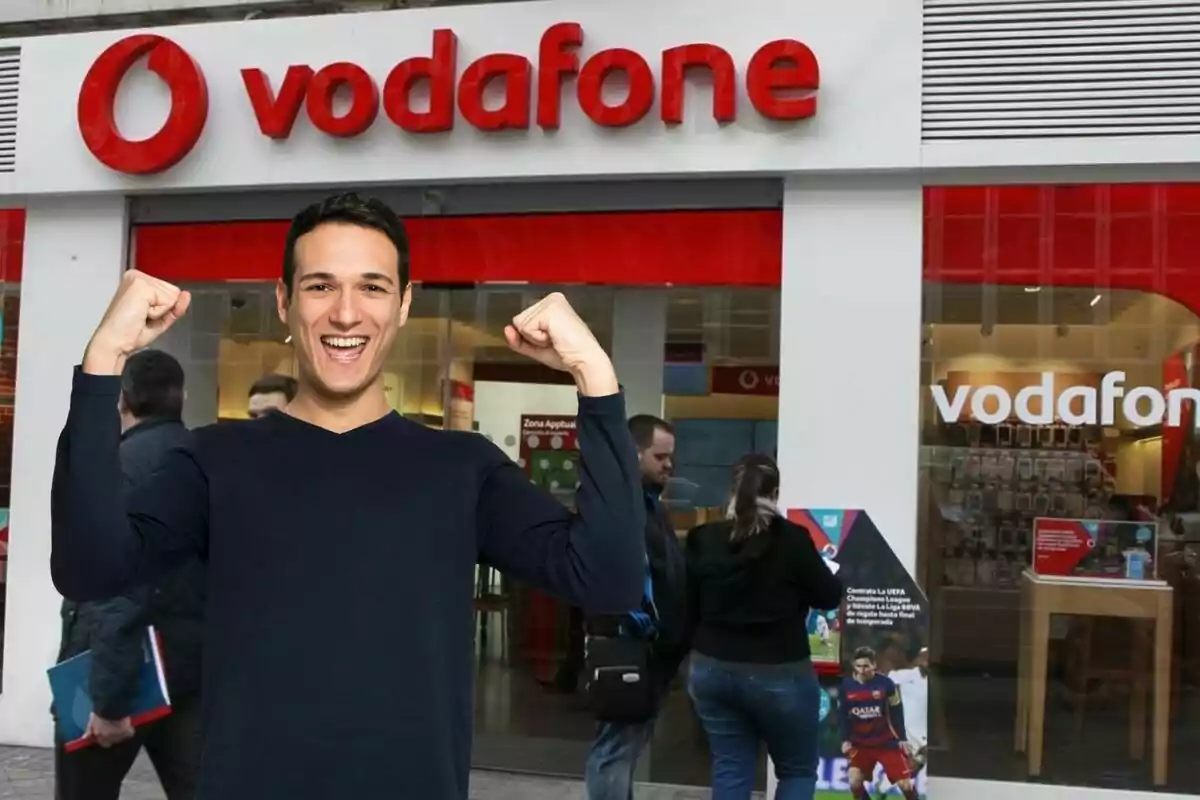 Un home somrient amb els braços aixecats davant d'una botiga de Vodafone.