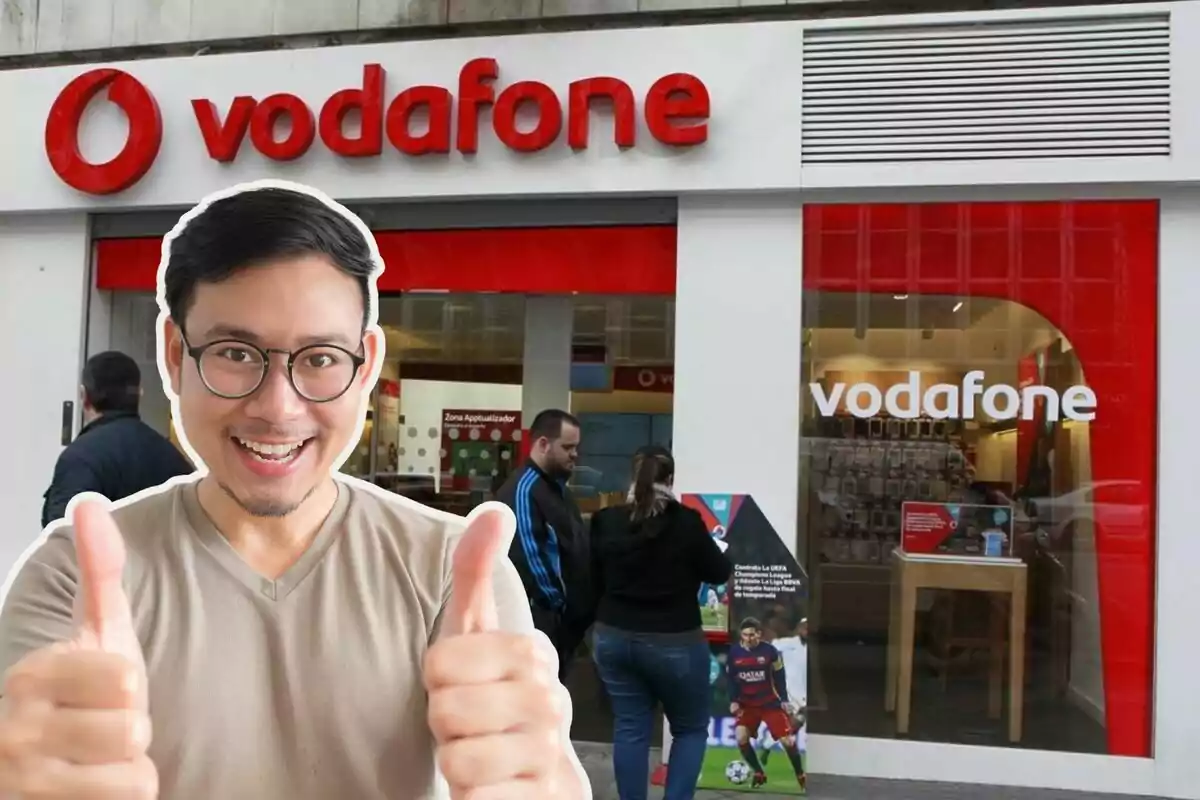 Un hombre sonriente con gafas y pulgares arriba frente a una tienda de Vodafone.