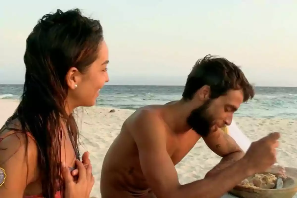 Anita i Montoya a la platja, una dona somriu mentre un home menja d'un plat, amb el mar de fons a 'Supervivientes'. Anita i Montoya a la platja, una dona somriu mentre un home menja d'un plat, amb el mar de fons a 'Supervivientes'.
