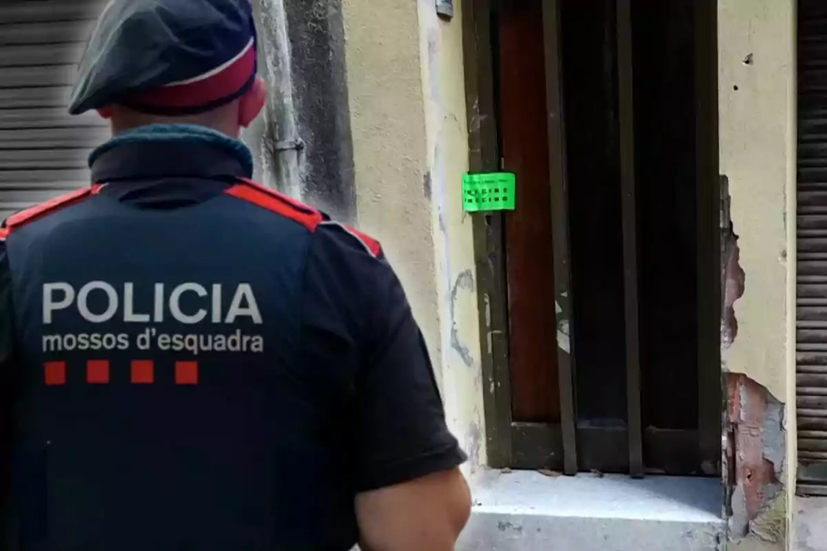 Un agent dels Mossos d'Esquadra davant d'una porta amb un cartell verd.