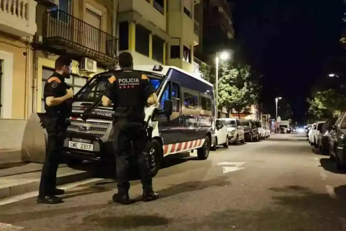 Two police officers next to a van on a street lit by streetlights at night.