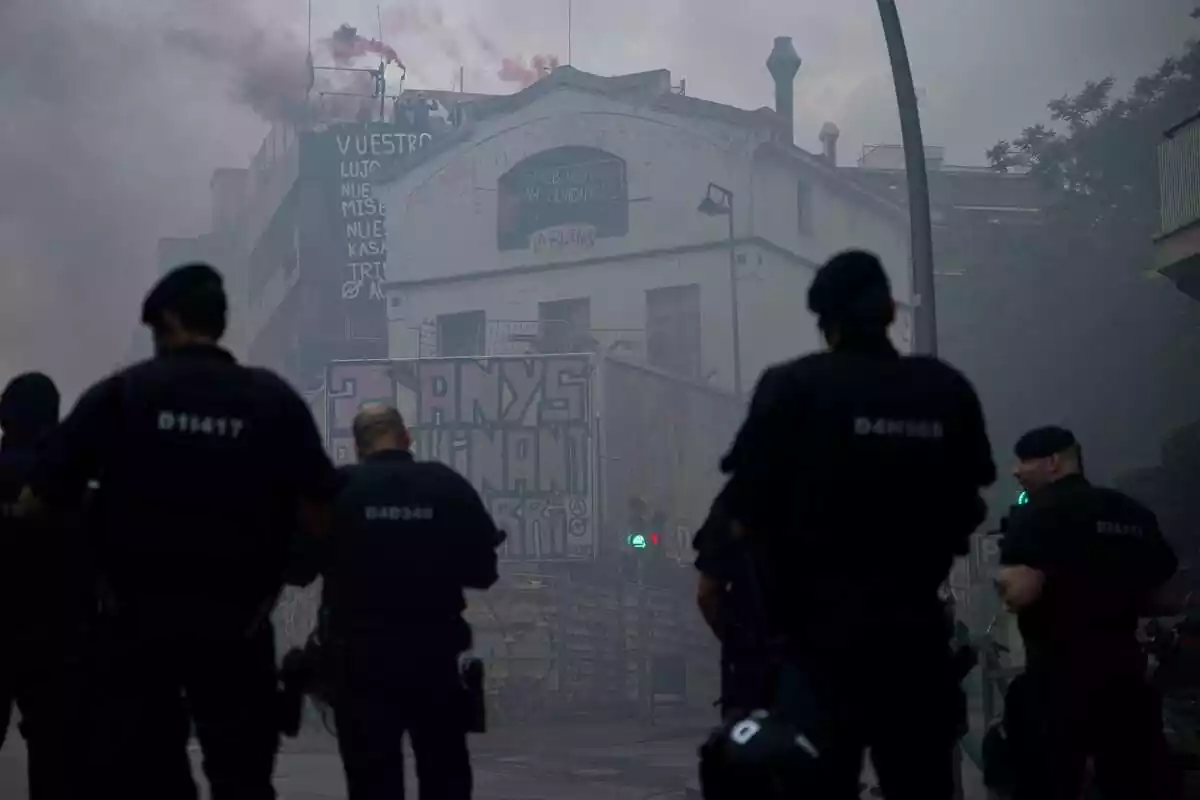 Diversos Mossos d'esquena mirant cap a les cases okupades La Ruïna i Kubo de la Bonanova amb molt de fum a l'aire