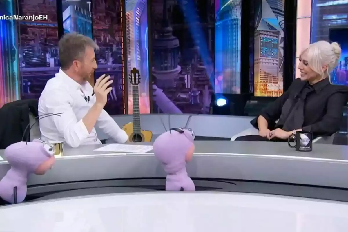 Pablo Motos i Mónica Naranjo conversen animadament a 'El Hormiguero', amb titelles porpres a la taula i una guitarra al fons. Pablo Motos i Mónica Naranjo conversen animadament a 'El Hormiguero', amb titelles porpres a la taula i una guitarra al fons.