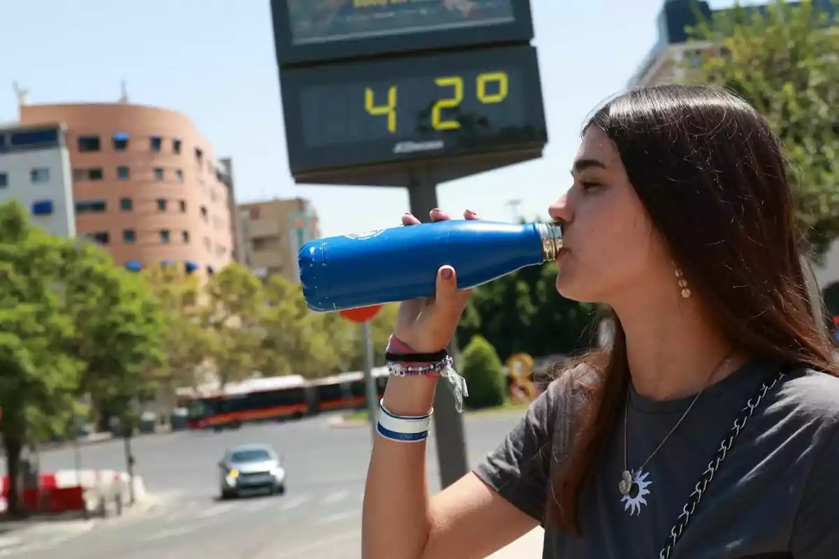 Jove bevent aigua d’una ampolla blava al carrer durant un dia calorós amb un termòmetre que marca 42 graus al fons. Jove bevent aigua d’una ampolla blava al carrer durant un dia calorós amb un termòmetre que marca 42 graus al fons.
