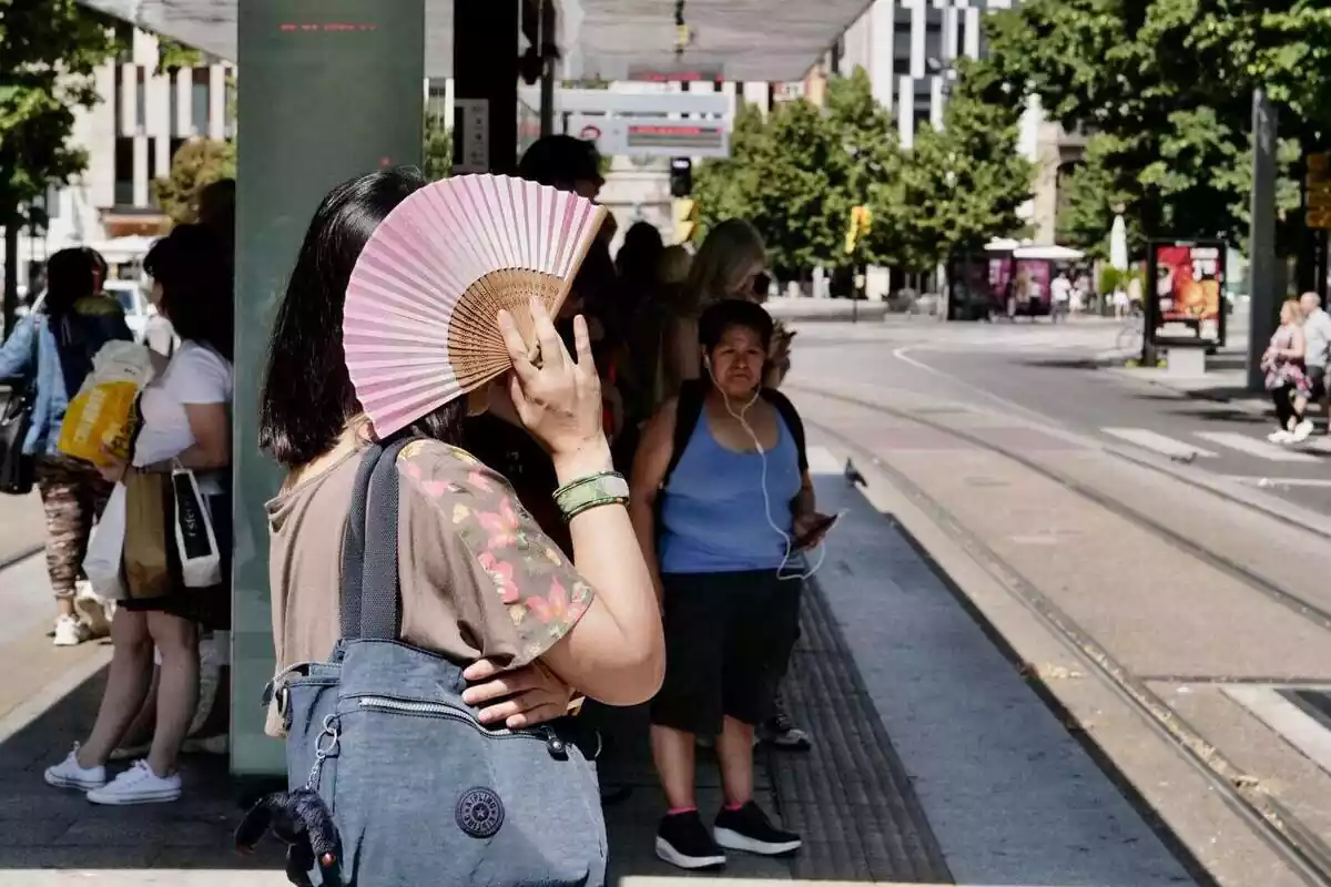 Un grup de persones esperant el tramvia en un dia de molta calor i una dona amb un ventall a la mà Un grup de persones esperant el tramvia en un dia de molta calor i una dona amb un ventall a la mà
