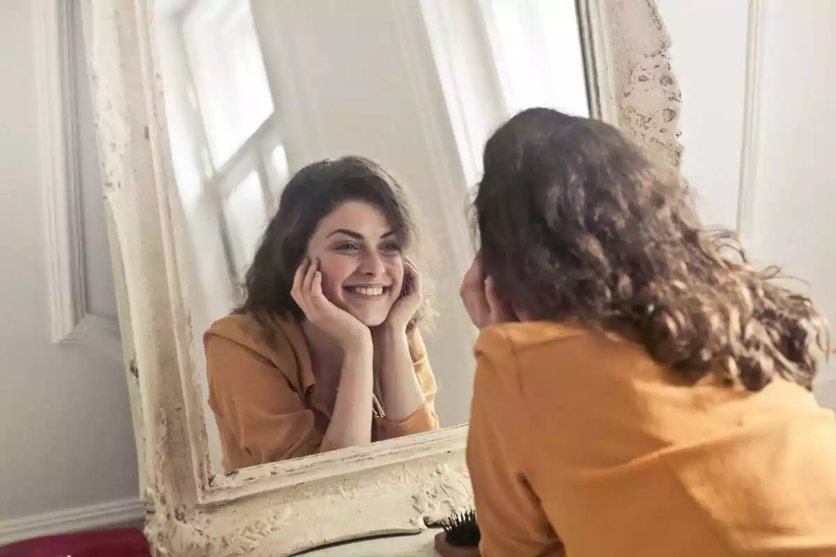 Dona amb pèl castany mirant-se al mirall mentre somriu feliçment