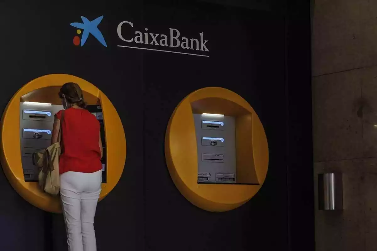 Una dona d'esquenes utilitzant un caixer automàtic de CaixaBank