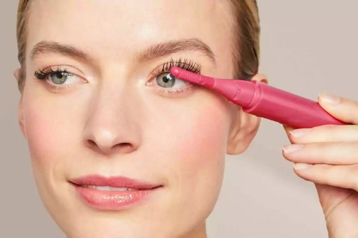 Woman using a pink Lidl electric eyelash curler on her left eye. Woman using a pink Lidl electric eyelash curler on her left eye.