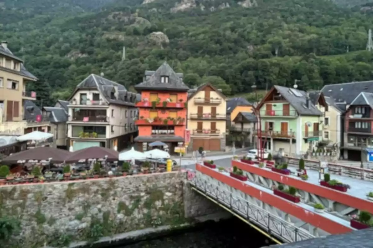 Un pintoresc poble amb cases acolorides i un pont sobre un riu envoltat de muntanyes i vegetació.