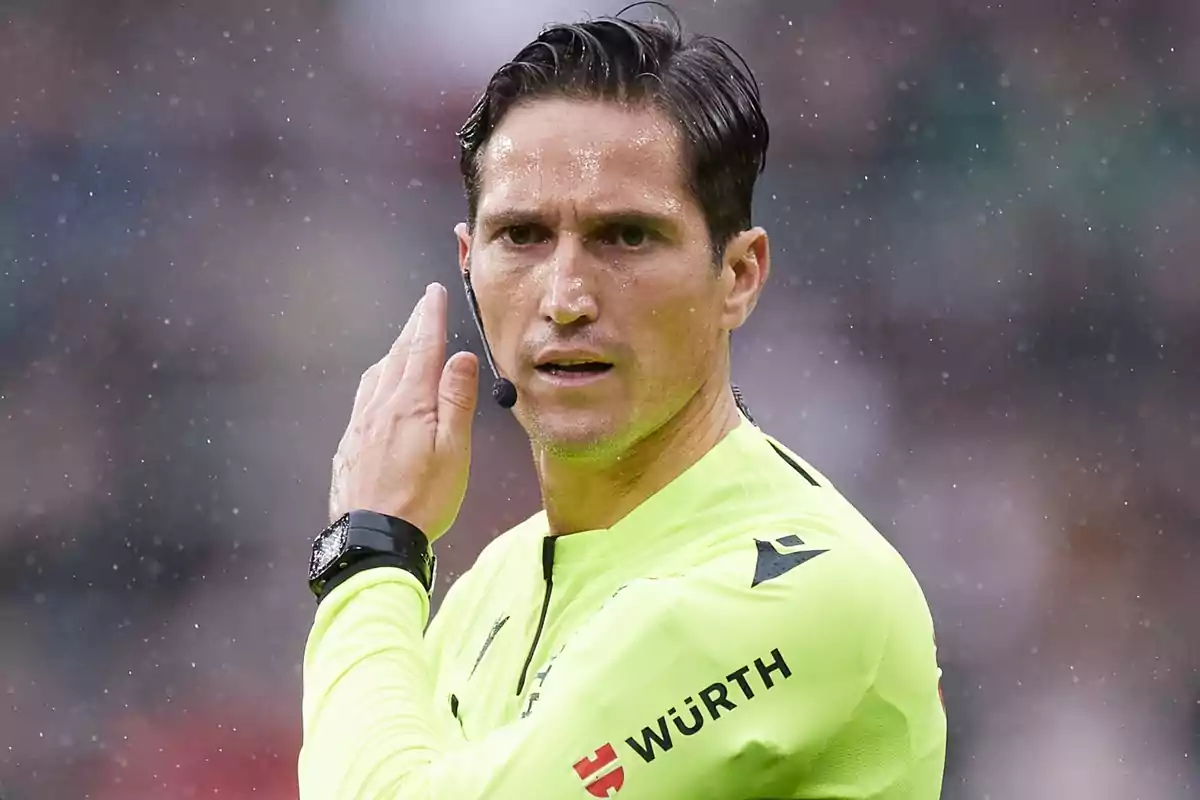 A soccer referee on the field with a yellow uniform and earpiece.