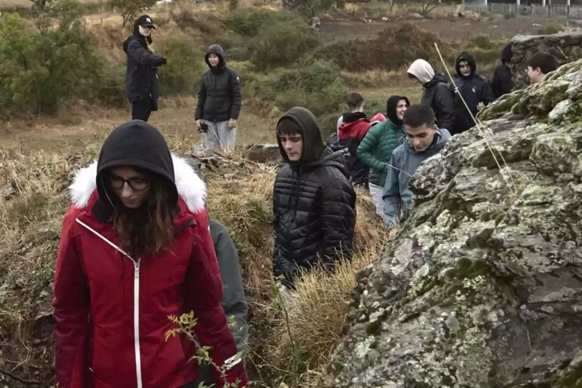 Un grup de persones amb roba d'abric caminen per un sender en un entorn natural, envoltat de vegetació i roques.