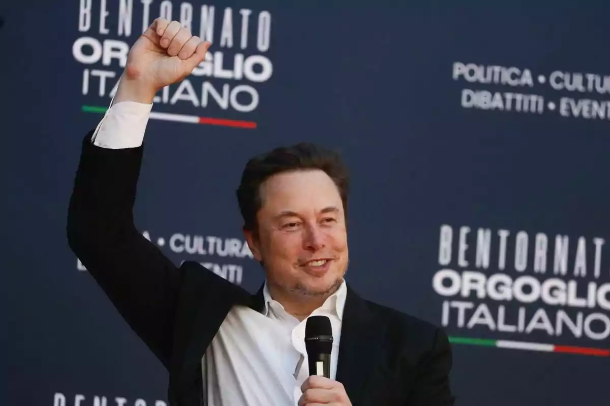 Elon Musk levantando el puño y sosteniendo un micrófono frente a un fondo con texto en italiano.