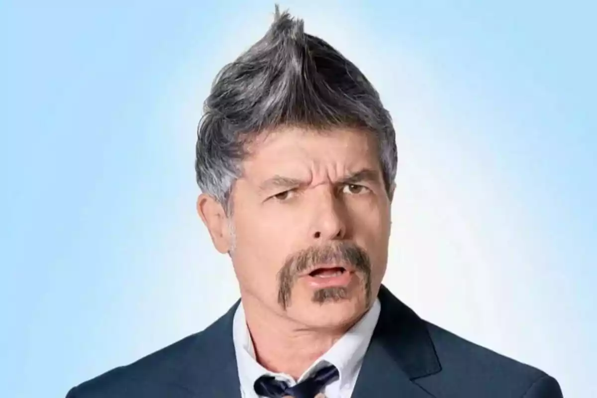 Man with a mustache and spiky hairstyle dressed in a suit and tie against a light blue background