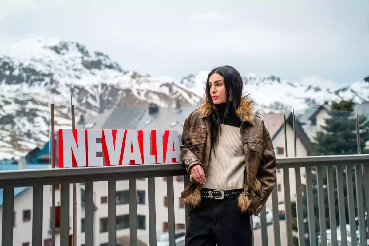 Natalia Lacunza con chaqueta de piel sintética y suéter claro está de pie junto a un letrero que dice "NEVALIA" con un paisaje montañoso nevado de fondo.