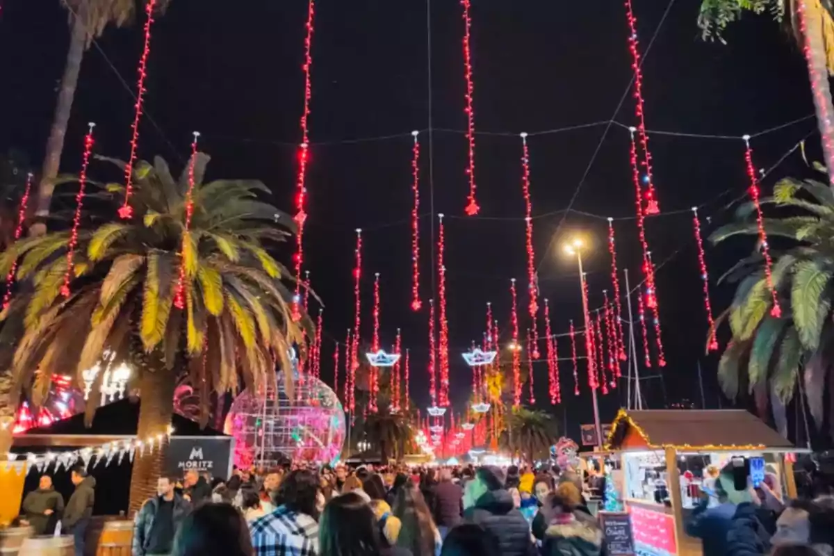 Una multitud gaudeix d´un mercat nocturn decorat amb llums vermelles penjants i palmeres il·luminades.