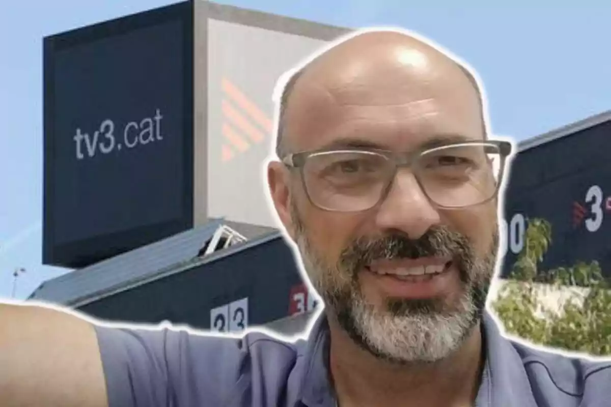 Un home amb ulleres i barba somriu davant d'un edifici amb el logotip de tv3.cat.