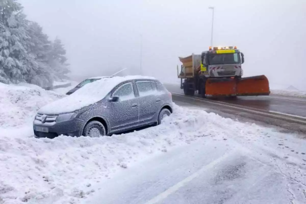 Una llevaneu circula per la carretera, amb un cotxe cobert de neu