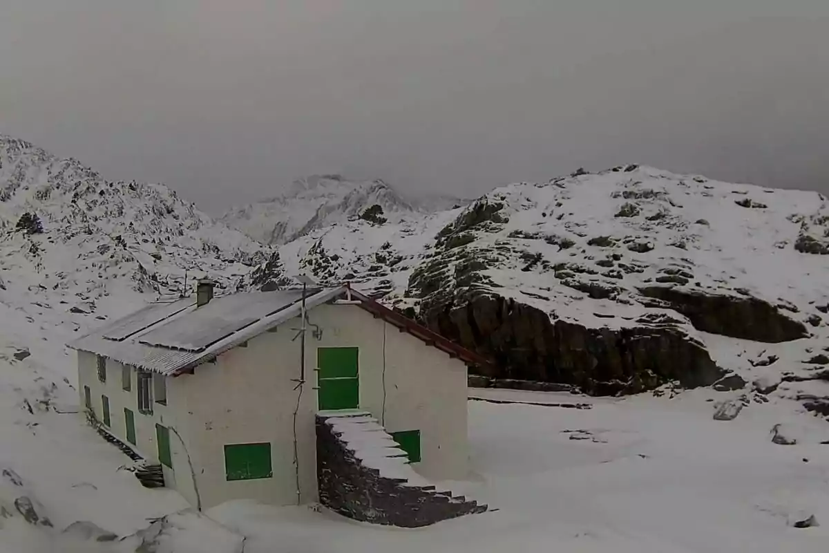 Una cabana blanca amb portes i finestres verdes es troba en un paisatge muntanyós cobert de neu.