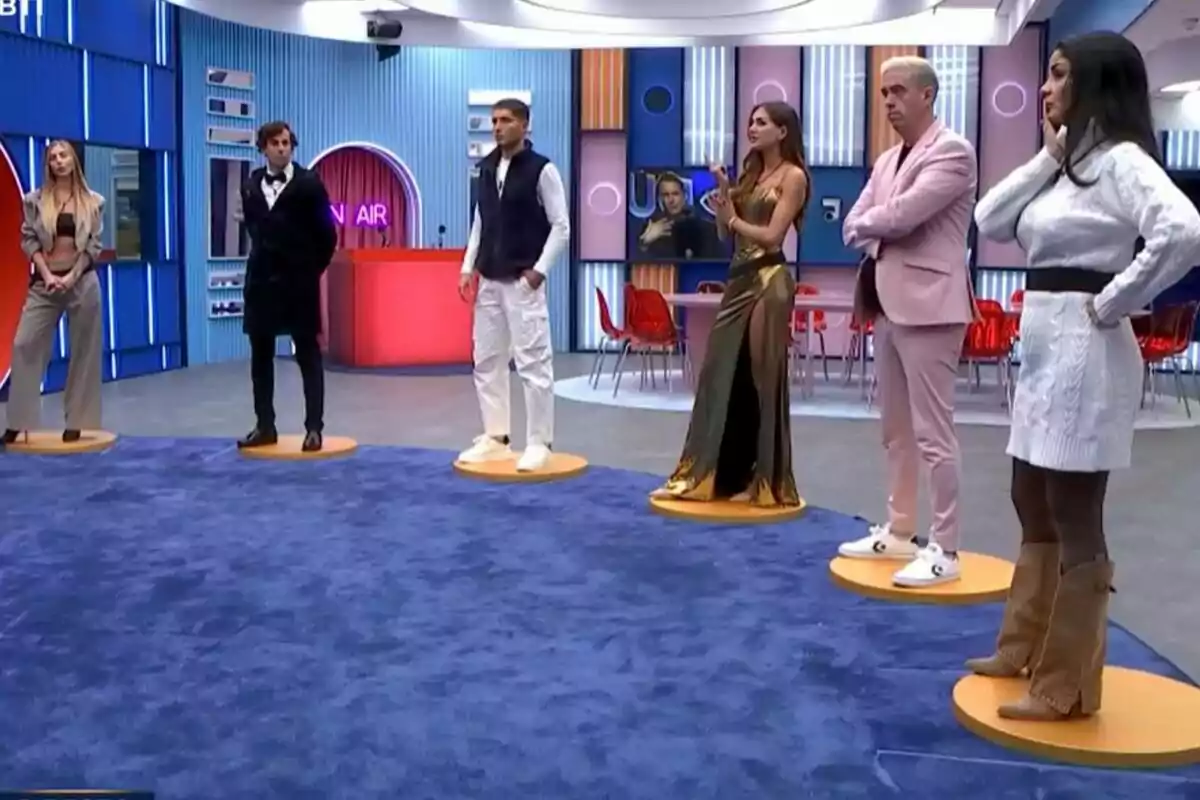 Ana Herminia, Javi Mouzo, Romina Malaspina, Óscar Landa y Maica Benedicto están de pie en la casa de GH DÚO con una alfombra azul y un fondo colorido.