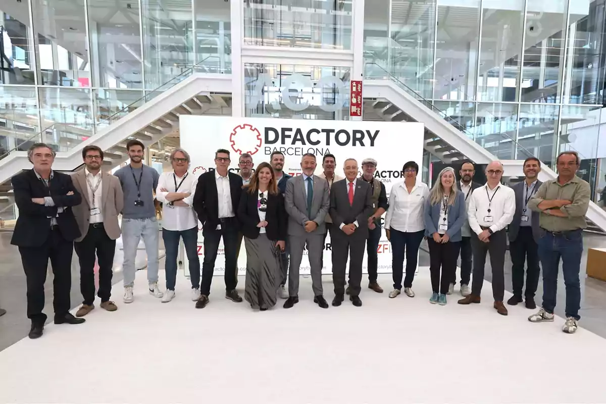 Un grup de persones posant davant d'un cartell que diu “DFactory Barcelona” en un entorn modern amb escales i parets de vidre.