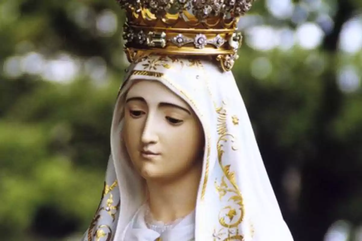 Una estàtua d'una figura religiosa amb una corona daurada i un mantell blanc decorat amb detalls daurats.