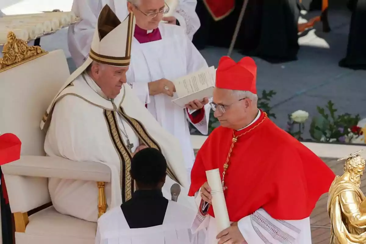 Un líder religiós assegut en una cerimònia mentre interactua amb un cardenal que sosté un document, acompanyat per assistents amb vestimenta litúrgica. Un líder religiós assegut en una cerimònia mentre interactua amb un cardenal que sosté un document, acompanyat per assistents amb vestimenta litúrgica.