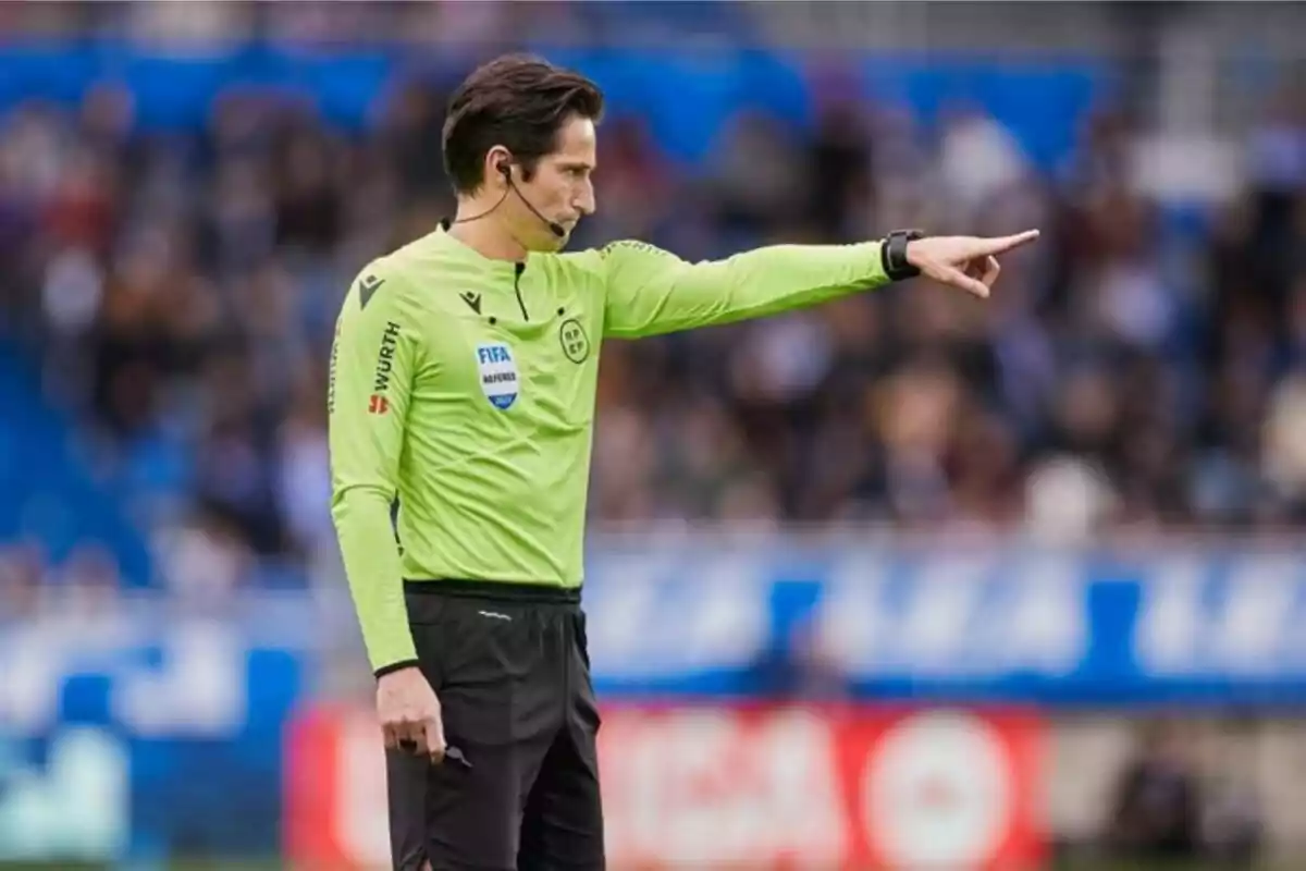 Un àrbitre de futbol amb uniforme verd assenyala amb el dit durant un partit.