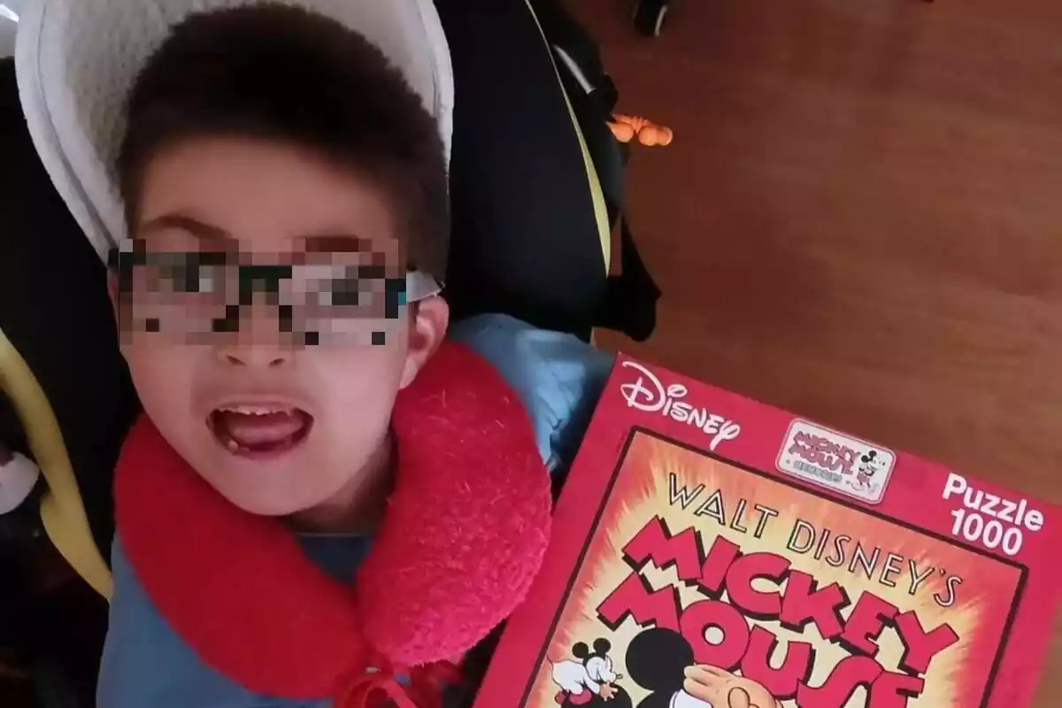 Pla curt d'Oliver, un nen que pateix Síndrome de West, amb rostre somrient, i un llibre de Mickey Mouse a la mà