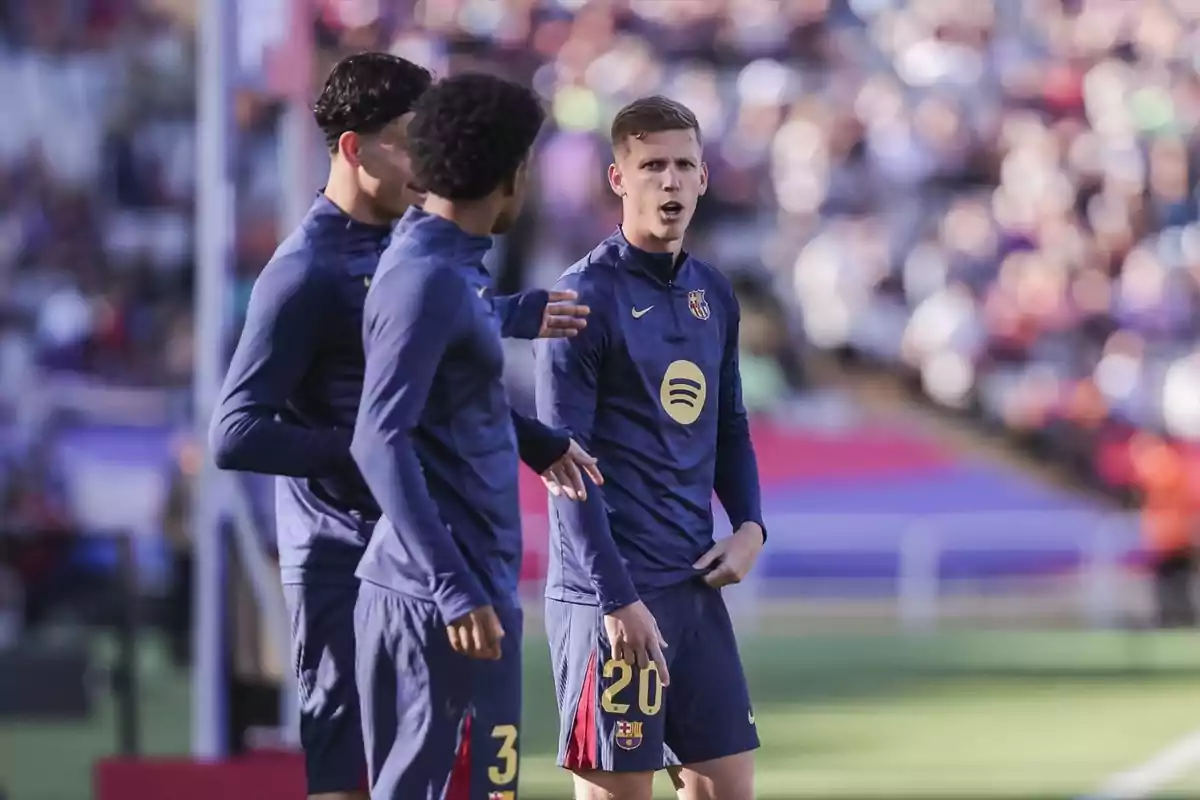 Tres jugadors de futbol del FC Barcelona conversen al camp durant un partit, vestint uniformes d'entrenament blau fosc. Tres jugadors de futbol del FC Barcelona conversen al camp durant un partit, vestint uniformes d'entrenament blau fosc.