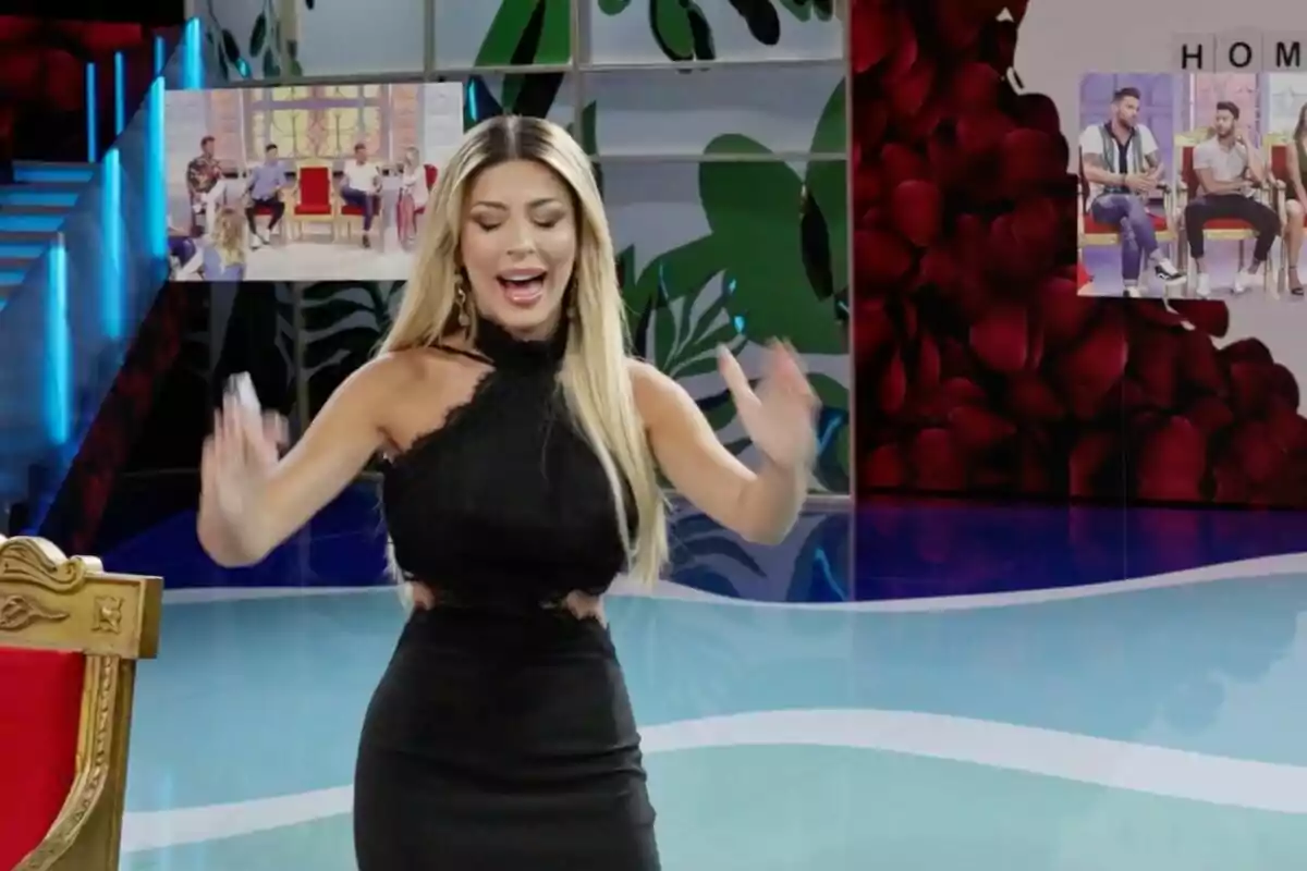 Oriana Marzoli amb vestit negre està gesticulant en un plató de televisió acolorit, amb pantalles al fons mostrant diverses persones assegudes. Oriana Marzoli amb vestit negre està gesticulant en un plató de televisió acolorit, amb pantalles al fons mostrant diverses persones assegudes.